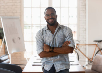 black man smiling arms folded desk in background bike leaning against wall