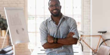 black man smiling arms folded desk in background bike leaning against wall