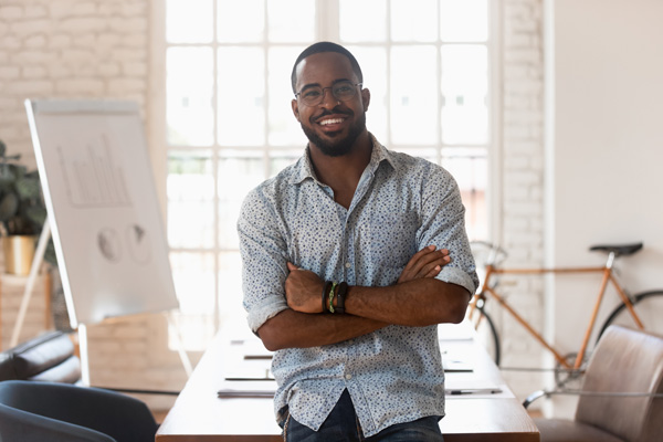 black man smiling arms folded desk in background bike leaning against wall