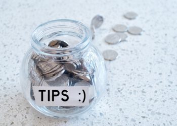 Glass jar with many coins and tips word over a marble counter top