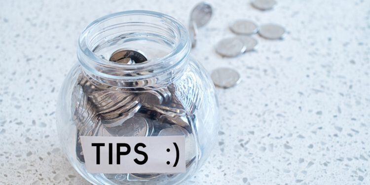 Glass jar with many coins and tips word over a marble counter top