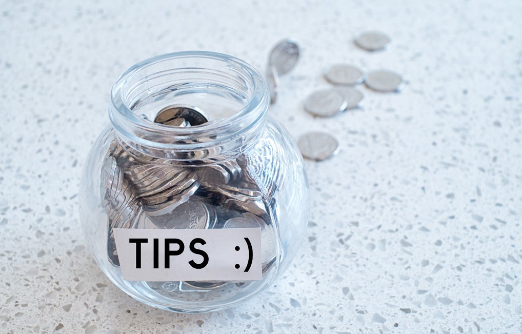 Glass jar with many coins and tips word over a marble counter top