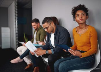 young african american woman feeling stressed about tedious waiting sitting in queue with other candidates for job interview