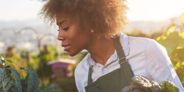 Black woman in green apron examining outdoor harvesting of plants